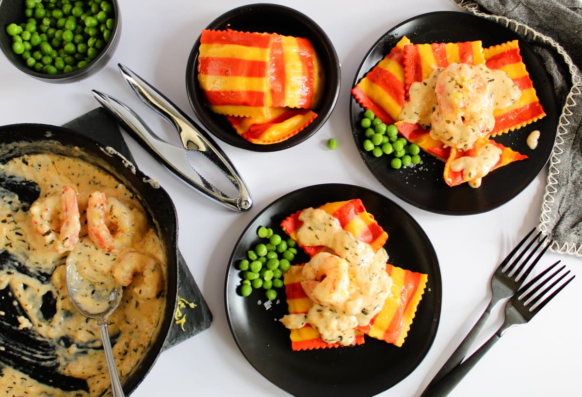 plates with lobster ravioli and cream shrimp sauce, green peas on side.